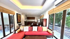 A modern living room with a sectional sofa, a wooden coffee table, and large windows offering views of the outdoors.