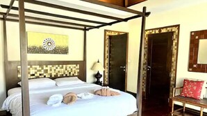A four-poster bed with a checkered headboard, a bedside table with a lamp, and a bench with a red cushion.