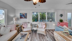 Una sala de estar con muebles de mimbre, ventilador de techo y ventanas amplias.