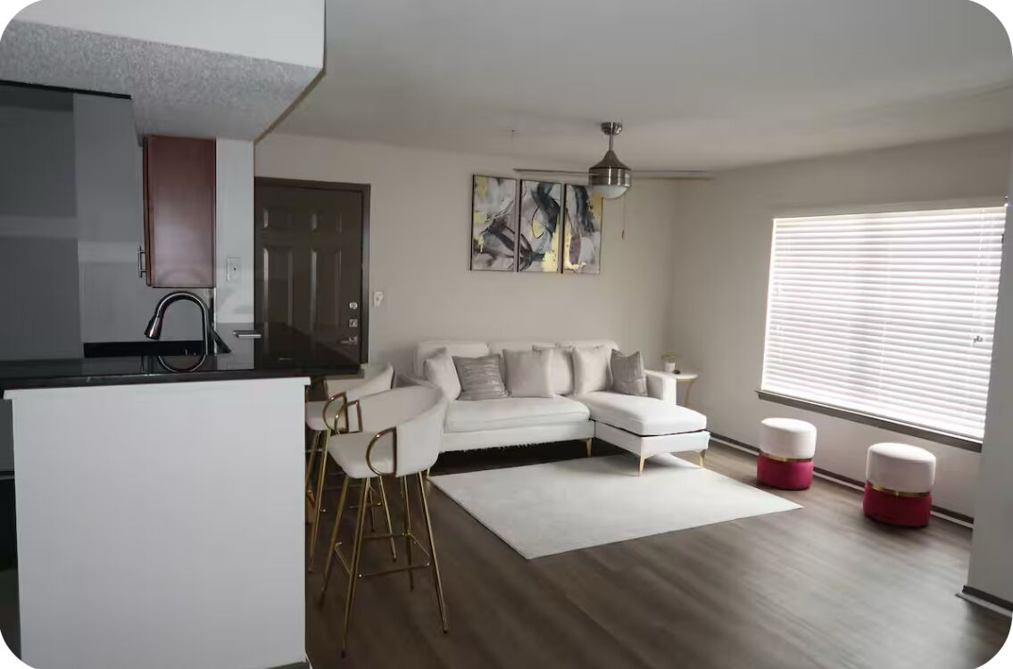 Una sala de estar moderna con un sofá seccional blanco, una mesita pequeña blanca y una zona de bar con taburetes.