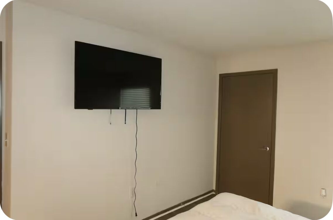 Une pièce avec un lit, une porte et un téléviseur fixé au mur.