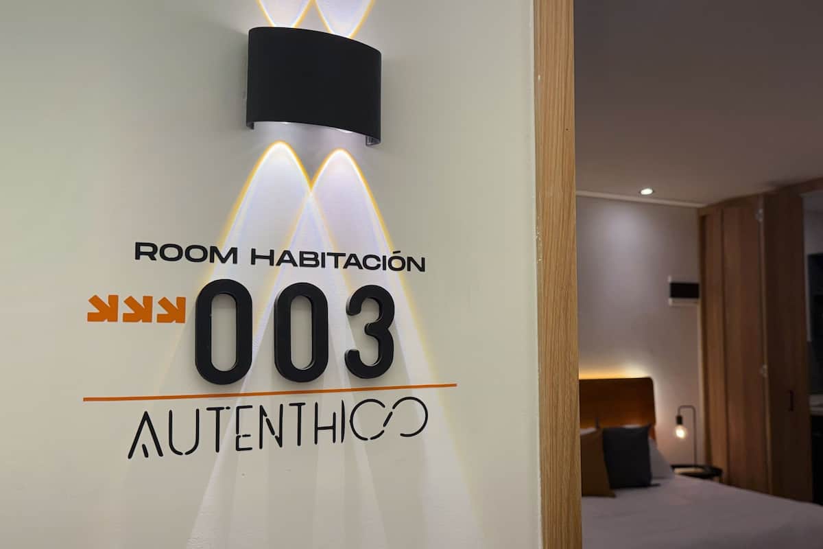 A hotel room sign with "ROOM HABITACIÓN 003" and "AUTENTHICO" indicating room number and brand.