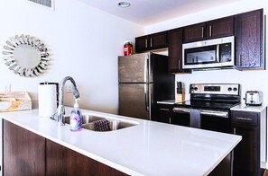 Una cocina moderna con armarios de madera oscura, electrodomésticos de acero inoxidable, una encimera blanca y un espejo decorativo.