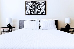 Habitación de hotel con una cama grande, dos mesitas de noche con lámparas y una obra de arte con estampado de cebra en la pared.