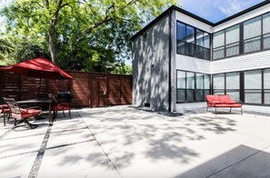 Una casa moderna con un patio, un comedor y un paraguas rojo para exteriores.