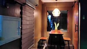 A modern kitchen with a dining area, featuring a central table with chairs, a hanging light fixture, and a potted plant.