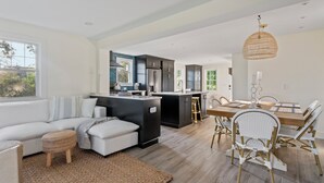 Une cuisine moderne avec des meubles de couleur sombre, un îlot central et un coin repas comprenant une table en bois et des chaises en osier.