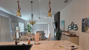 A modern kitchen with a granite countertop, a sink, and a dining area with a table and chairs. There are pendant lights above the kitchen and a fireplace in the dining area. - Beautiful, well appointed, 3-bed house in DeLuna - 2 Kings! (The Villages)