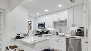 A modern kitchen with white cabinets, a central island, stainless steel appliances, and a black trash bin.