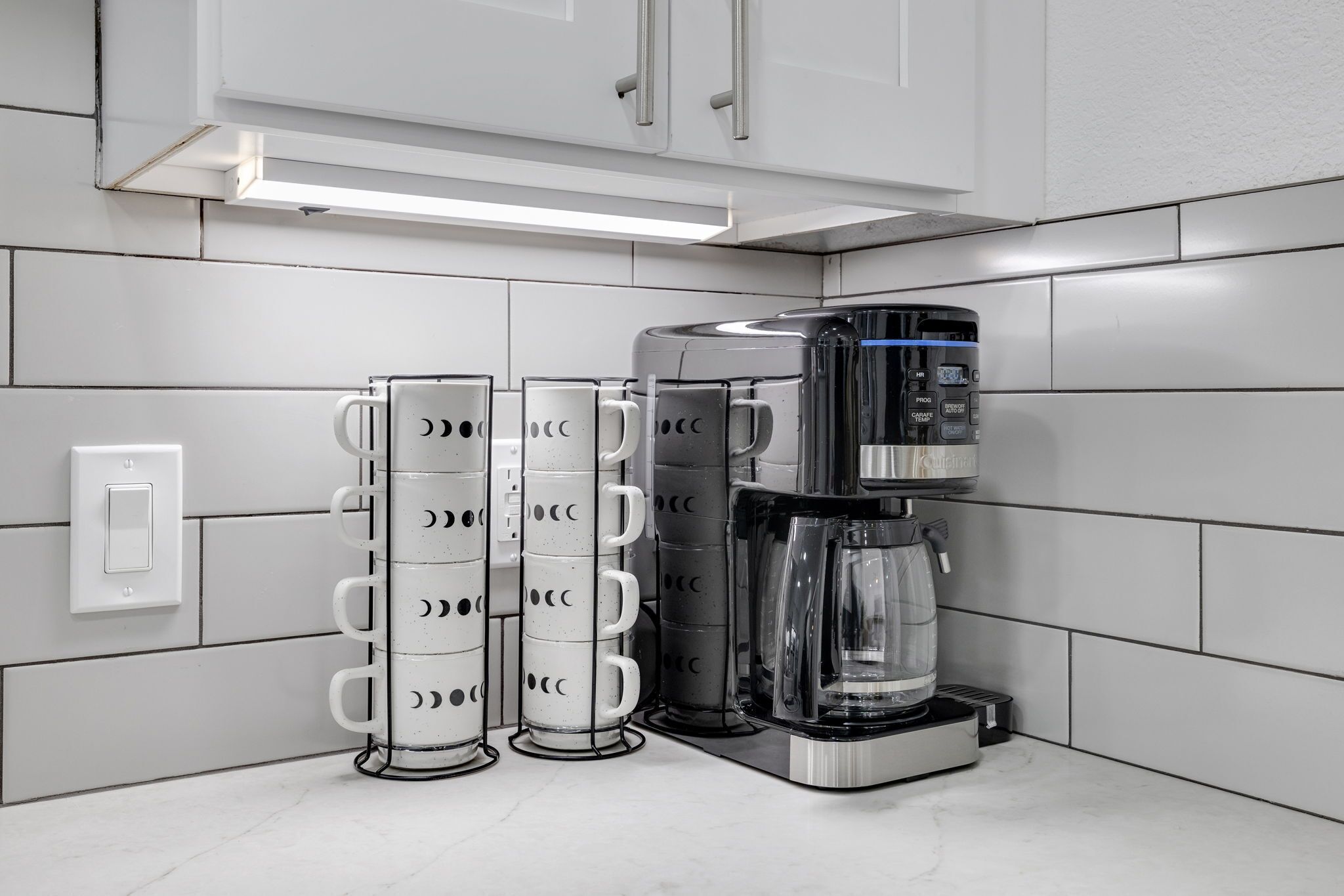 Une cuisine avec des meubles blancs, une machine à café et un porte-tasses.