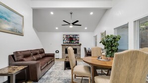 A living room with a brown leather sofa, a wooden dining table with chairs, a fireplace, and a ceiling fan.