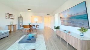 A modern living room with a dining area, a kitchen in the background, and a large beach-themed painting on the wall. - Top Location Waterfront Balcony Dream (North Miami Beach)