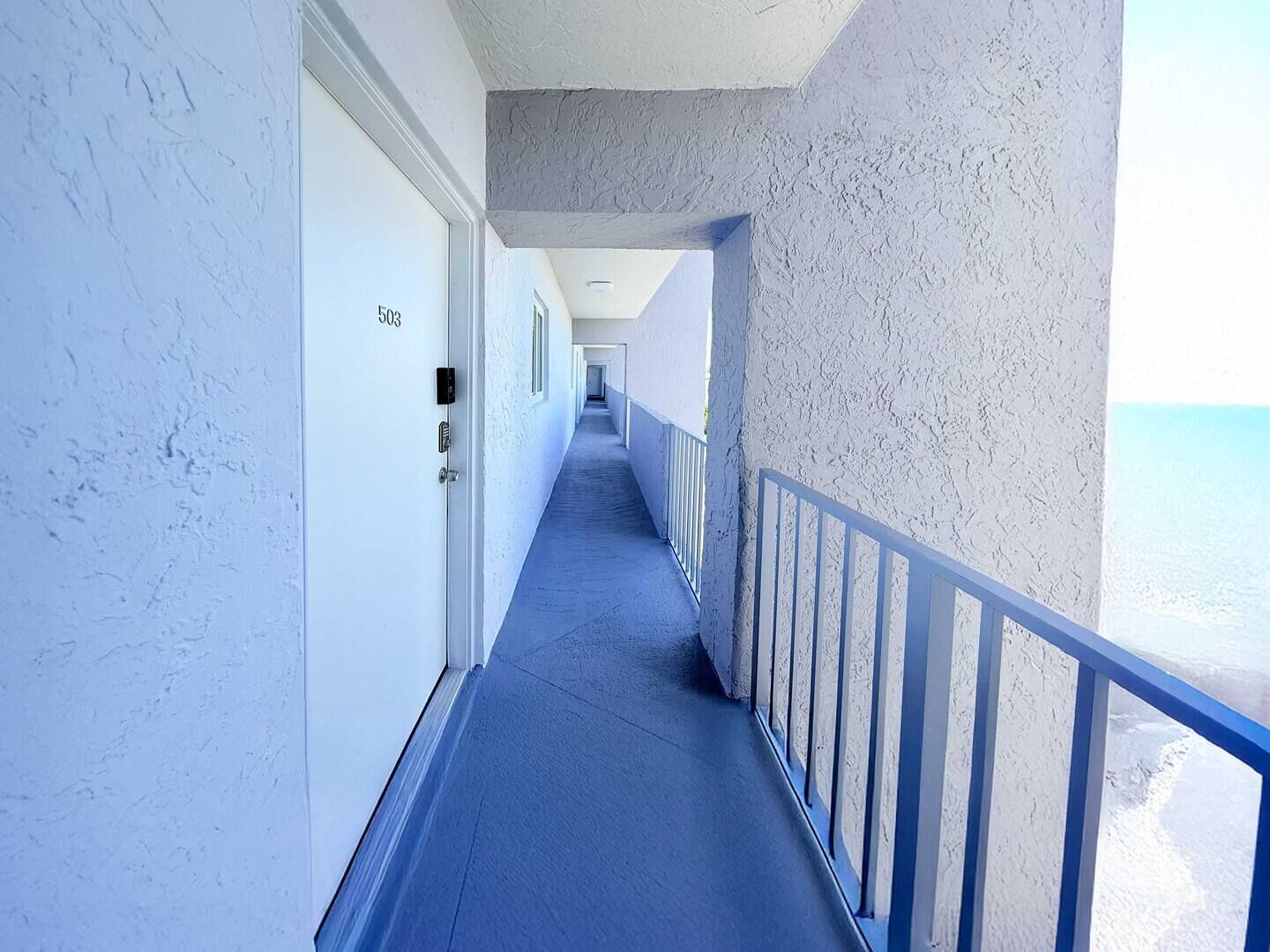 Um corredor com piso azul, paredes brancas e guarda-corpo de varanda.