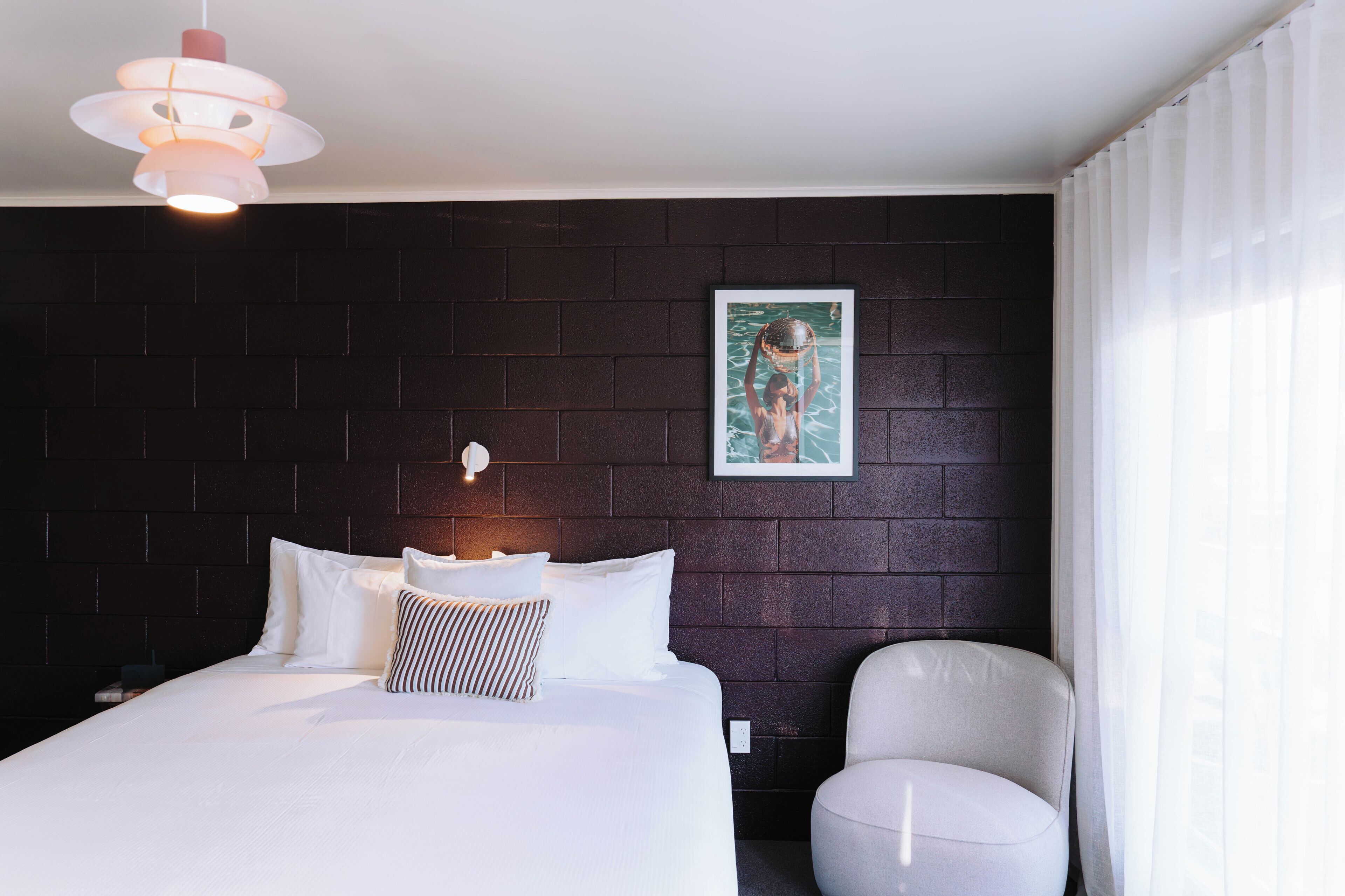 A hotel room with a bed, a chair, a wall-mounted picture, and a pendant light.