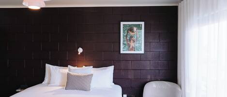 A hotel room with a bed, a chair, a wall-mounted picture, and a pendant light.