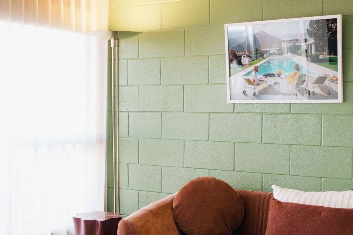 A living room with a green brick wall, a brown sofa, a glass coffee table, and a framed picture on the wall.