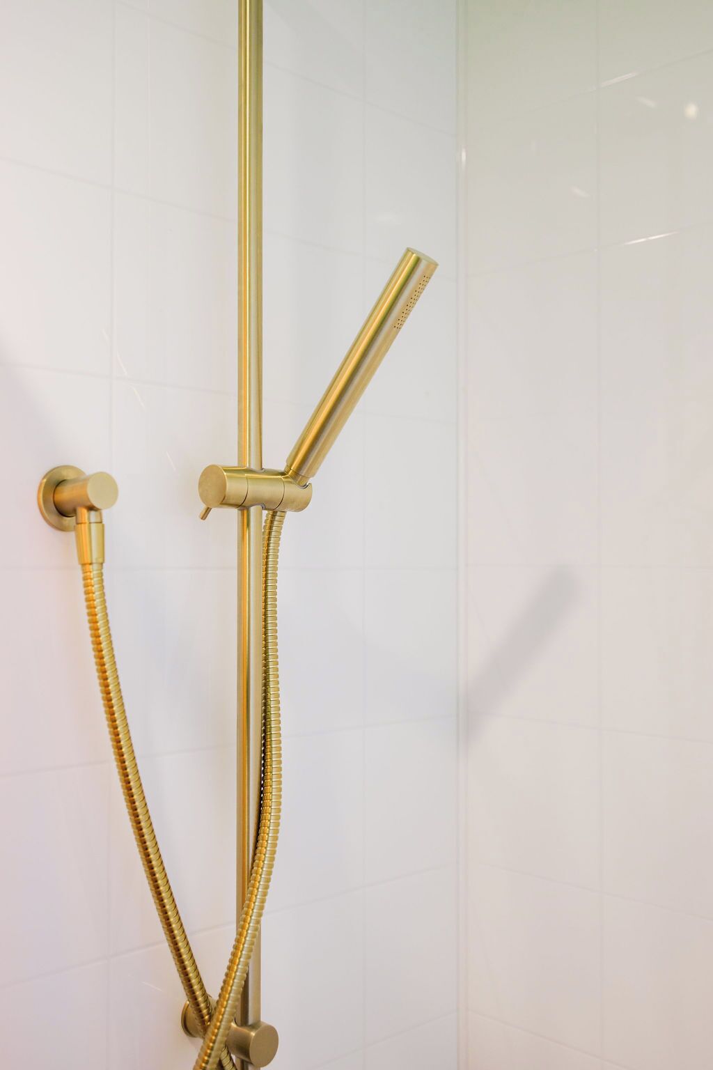 A gold showerhead with a flexible hose attached to a vertical pole, mounted on a white tiled wall.