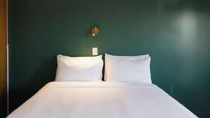 A neatly made bed with white linens in a room with dark green walls. - The Mayfair (Hastings)