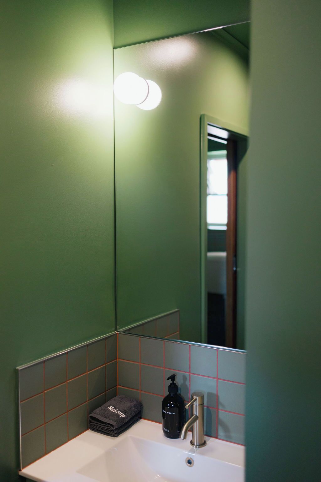 Ein Badezimmer mit grüner Wand, weißem Waschbecken, Spiegel und Handtuch.