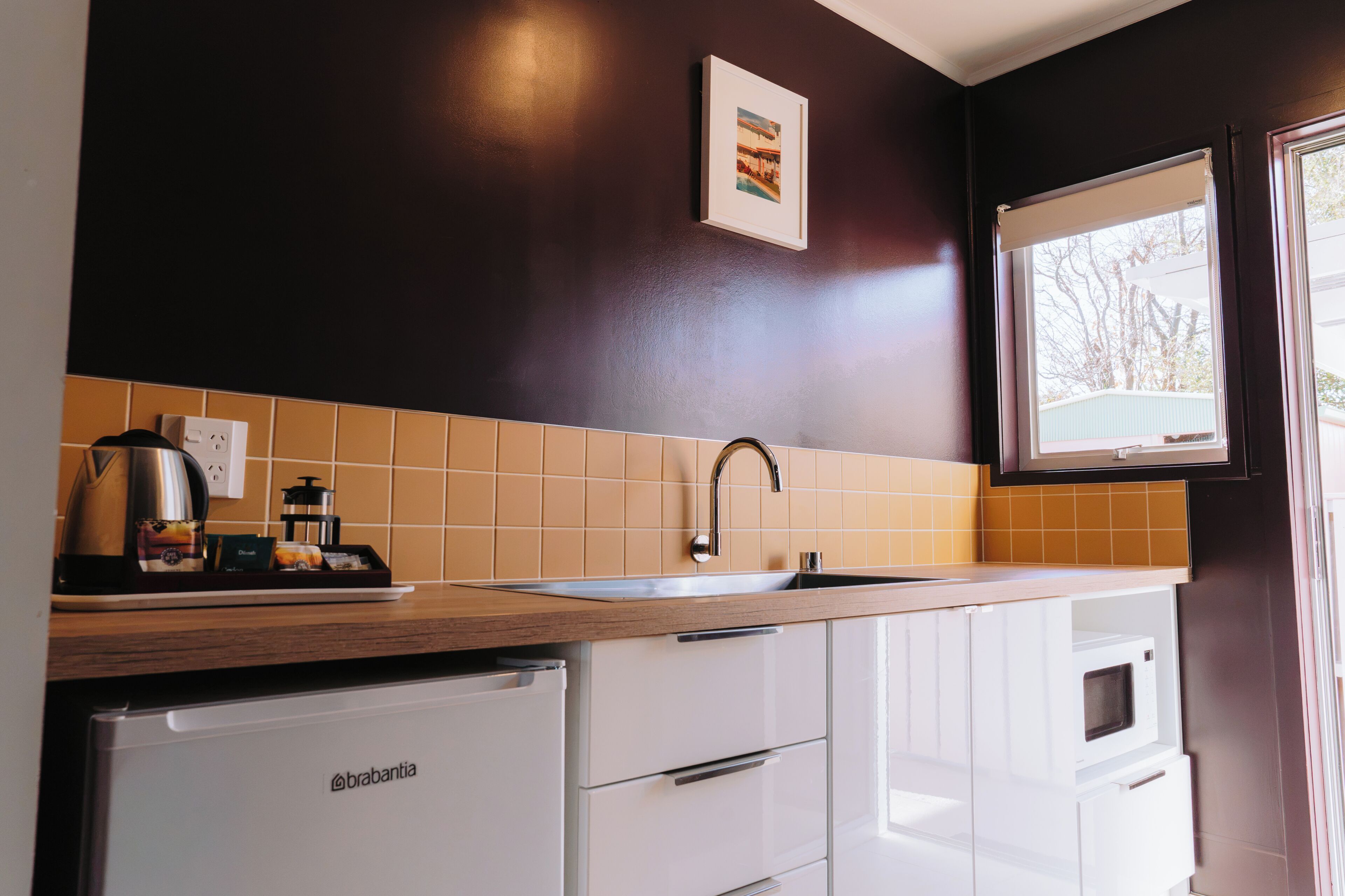 Una cocina con un lavamanos, una cafetera y un refrigerador.