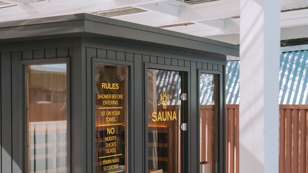 A sauna with clear glass doors, a wooden bench outside, and a list of rules on the glass. - The Mayfair (Hastings)