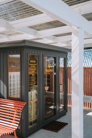 A sauna with clear glass doors, a wooden bench outside, and a list of rules on the glass. - The Mayfair (Hastings)