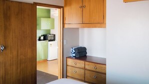 A hotel room with a wooden wardrobe, a bed, and a kitchenette in the background. - The Mayfair (Hastings)