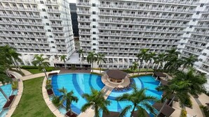 A large, multi-level hotel with a central swimming pool surrounded by palm trees and lounge areas.