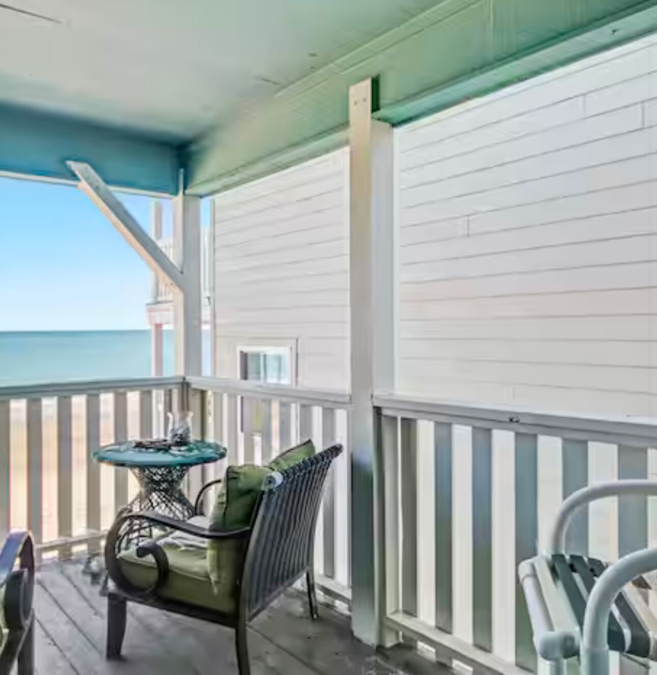A covered porch with a view of the ocean, a table with chairs, and a railing.