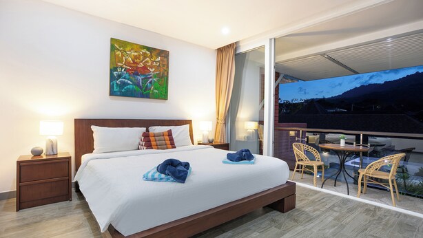 Habitación de hotel con una cama grande, un cuadro en la pared, un balcón con mesa y sillas, y vistas a las montañas.