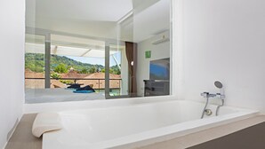 Un baño moderno con una bañera grande, ducha y vistas a un paisaje verde a través de un ventanal amplio.