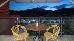 Un balcón con una mesa redonda de madera y dos sillas de mimbre, con vistas a un paisaje montañoso.