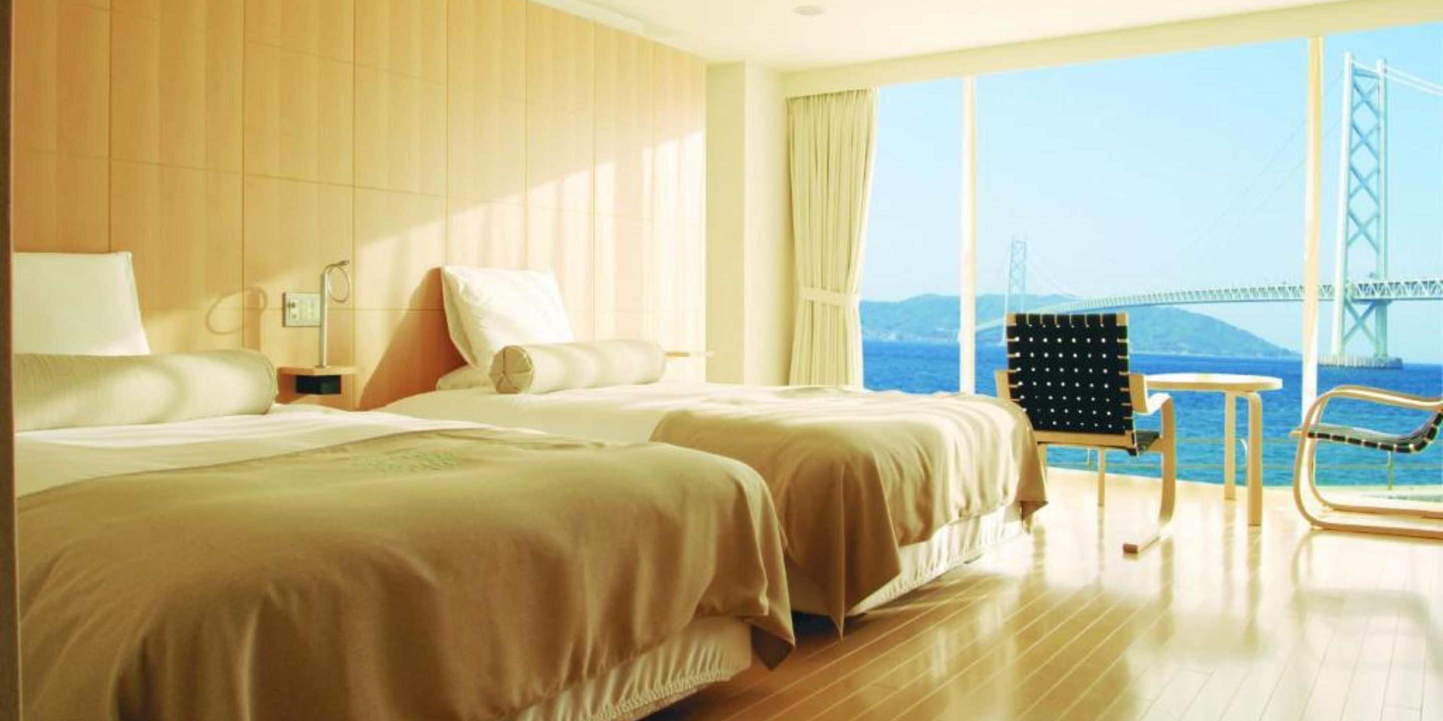 A hotel room with two beds, a view of a bridge, and a chair by the window.