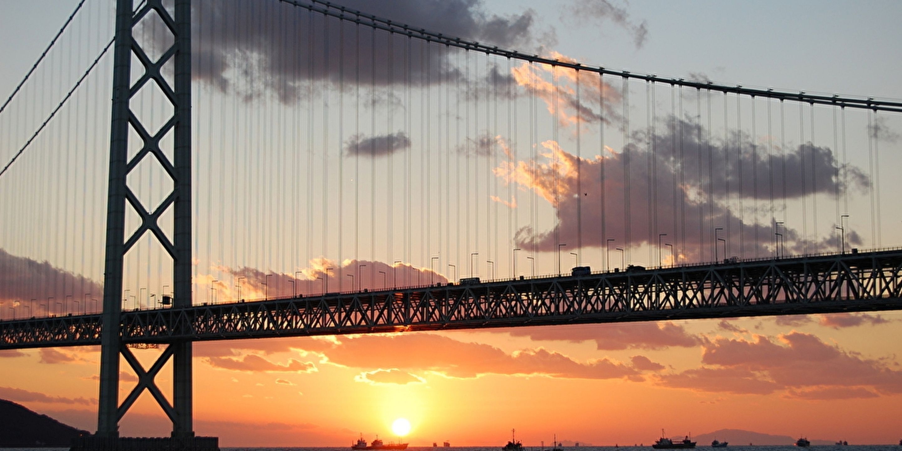 Un puente colgante con un atardecer de fondo.