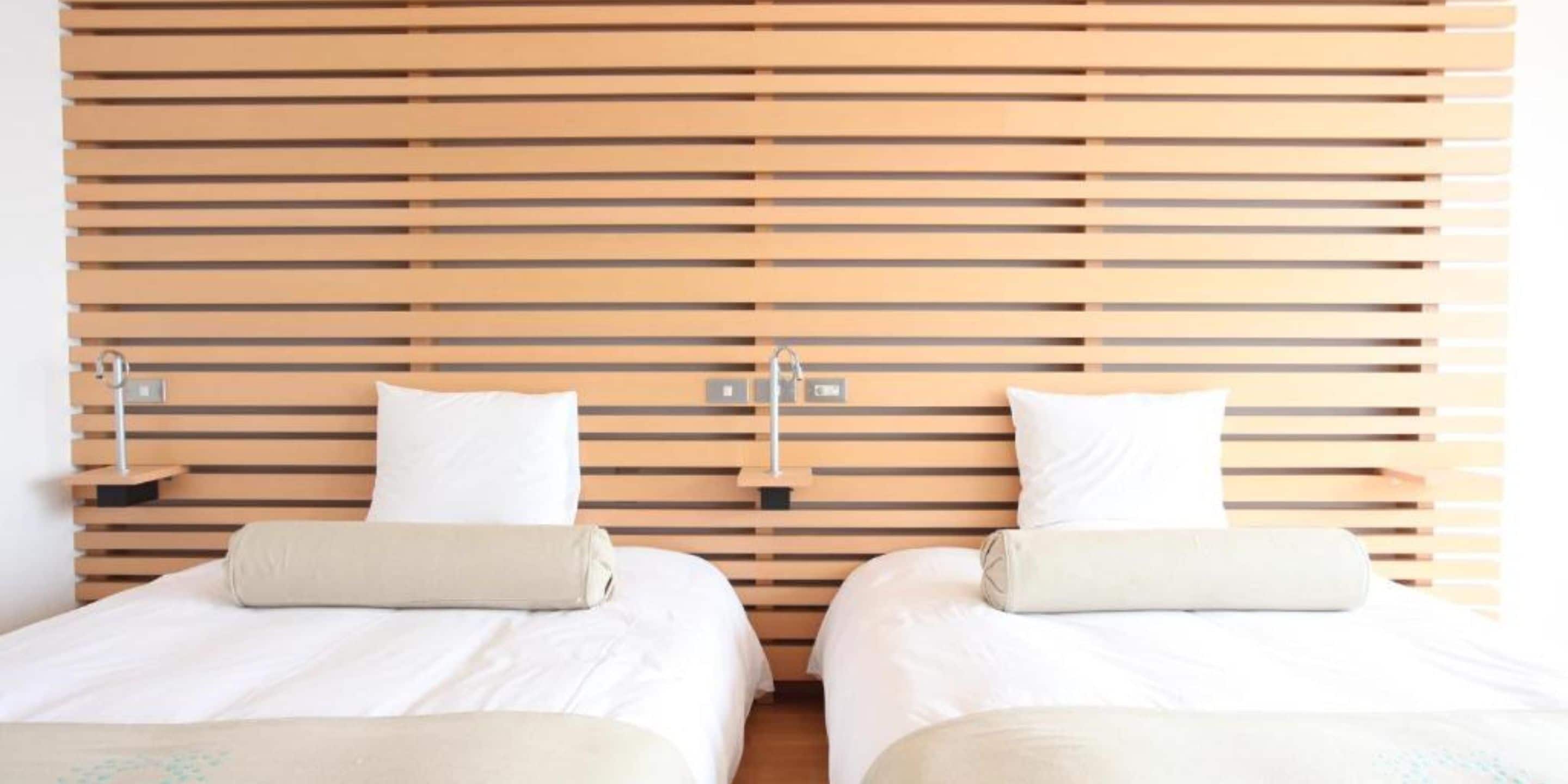 A hotel room with two beds, wooden slat headboards, bedside tables with lamps, and white bedding.