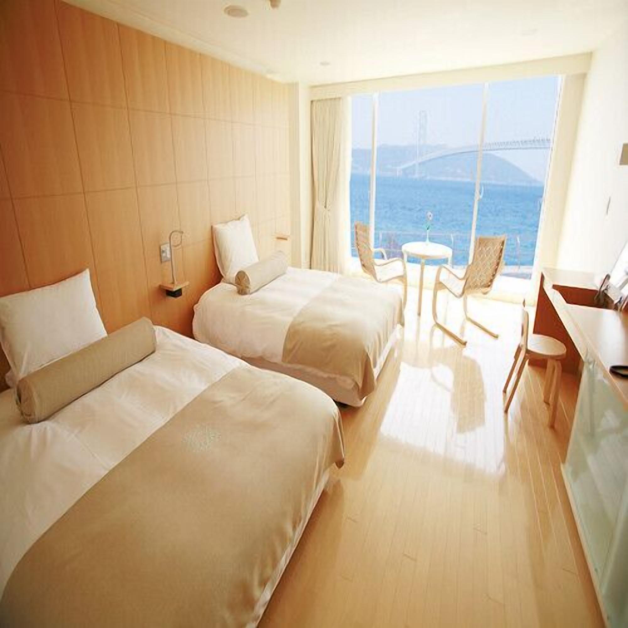 A hotel room with two beds, a small table, chairs, and a view of the sea.