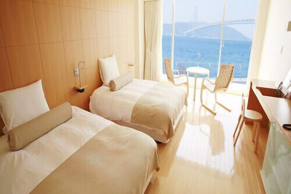 Une chambre d’hôtel avec deux lits, une petite table, des chaises et une vue sur la mer.