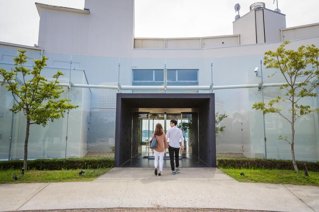 A modern building entrance with glass doors, a pathway, and small trees.