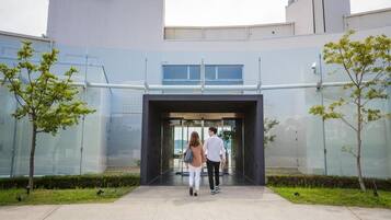 A modern building entrance with glass doors, a pathway, and small trees.