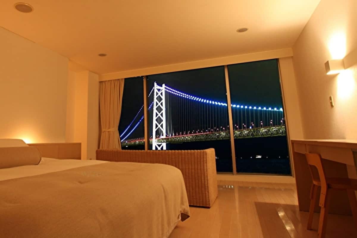 Une chambre d’hôtel avec un grand lit, un bureau et une vue sur un pont la nuit.