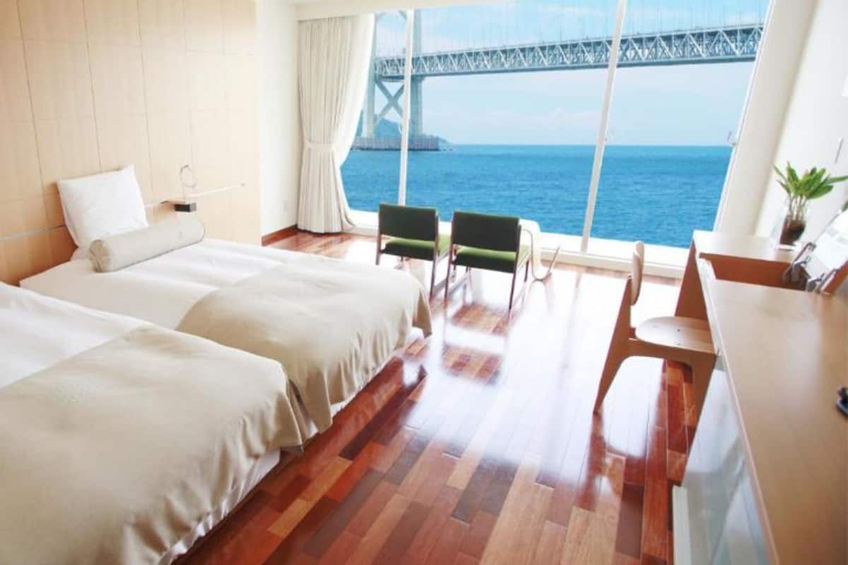 Une chambre d’hôtel avec deux lits, un bureau, une chaise et une vue sur un pont enjambant une étendue d’eau.