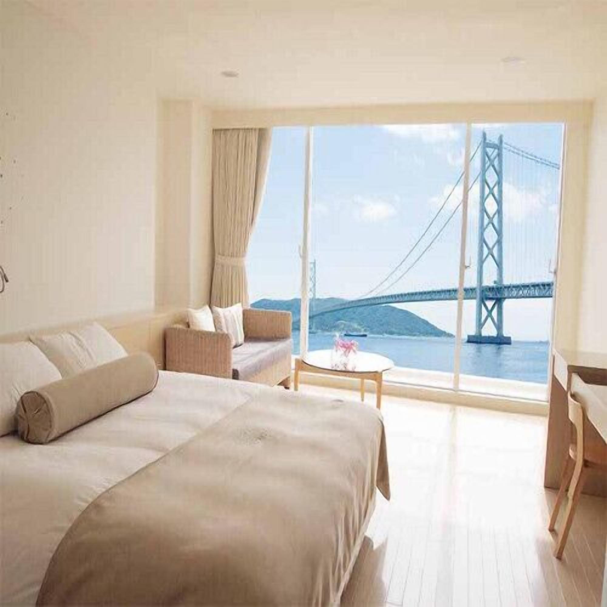 A hotel room with a large bed, a sofa, a small table, and a view of a bridge.