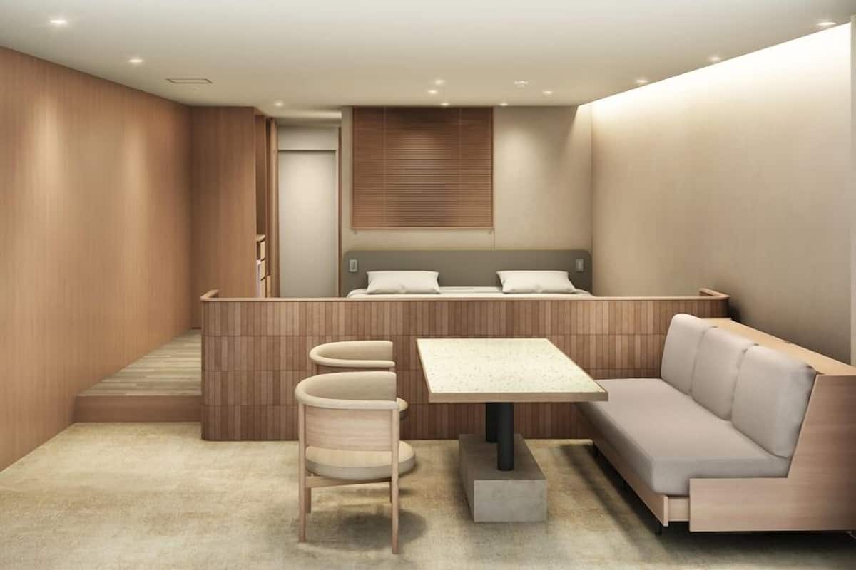 A modern hotel room with a sofa, a small table, a chair, and a bed with a headboard.