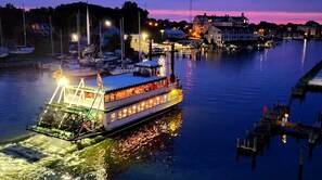 A riverboat docked at a marina with a waterfront view, surrounded by buildings and other boats.