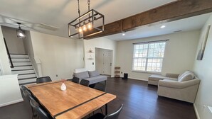 A spacious living area with a wooden dining table, black chairs, a grey sofa, a beige sofa, and a staircase leading to another level.