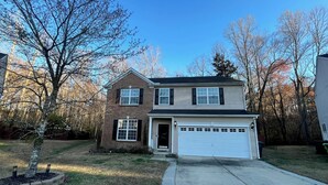 A two-story house with a garage, a brick exterior, and a front yard with a tree and a small garden.