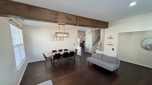 A spacious living area with a dining table, sofas, and a staircase leading to an upper floor.