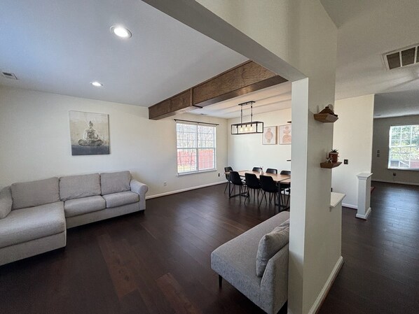 A spacious living area with a sectional sofa, a dining table with chairs, and a kitchen area visible through an open doorway.