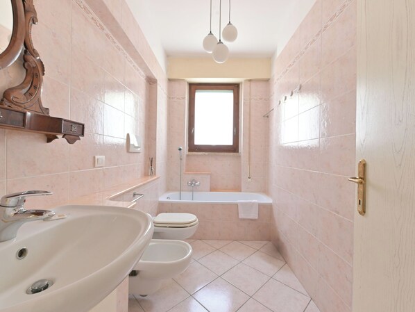 Un baño con lavabo, dos inodoros, bañera y ventana.