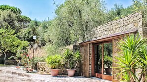 A stone-paved courtyard with potted plants and a wooden structure with glass doors. - Villa Anna by Interhome (Castiglione della Pescaia)
